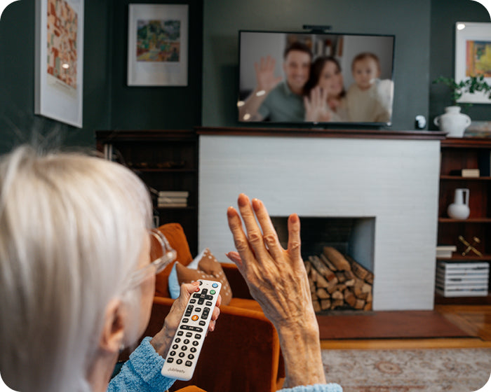 an elderly woman waving at the television on a video call on her tv with her family