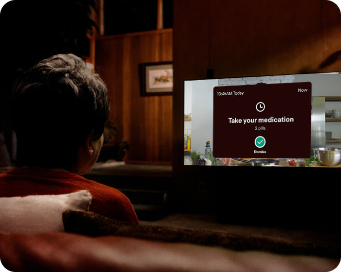 elderly woman watching tv and a medication reminder showing on the television